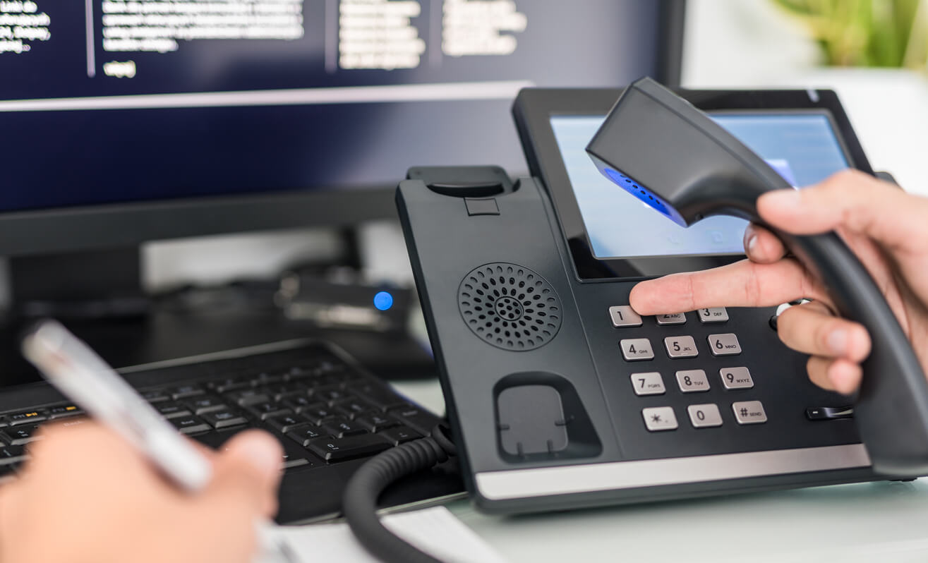 A close up shot of someone using a landline phone in an office environment